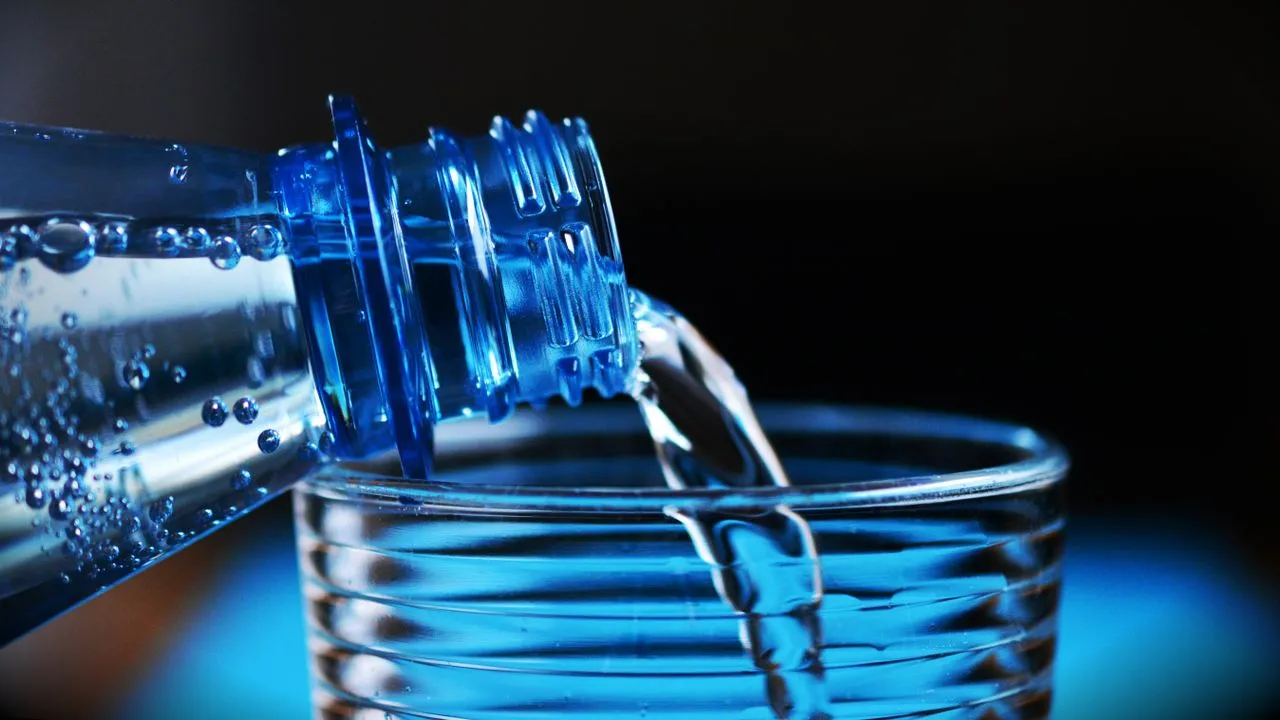 Agua sirviéndose desde una botella hacia un vaso de vidrio