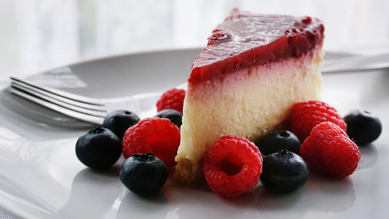 Porción de cheesecake con cobertura de frutos rojos en un plato blanco