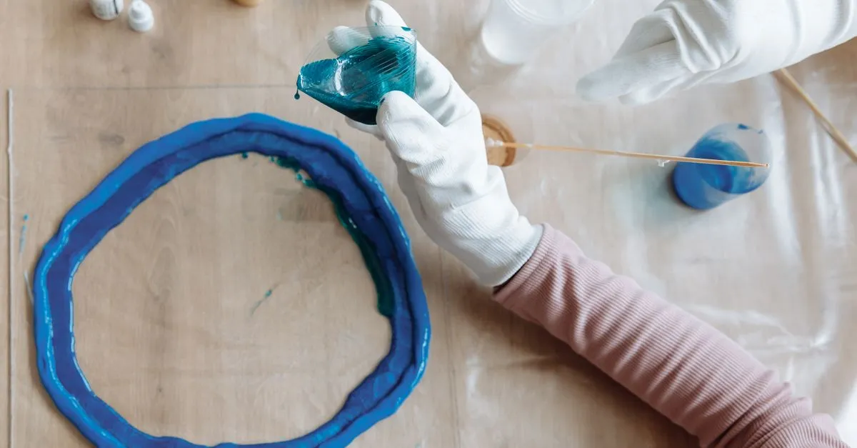 Manos con guantes vertiendo resina azul en un molde